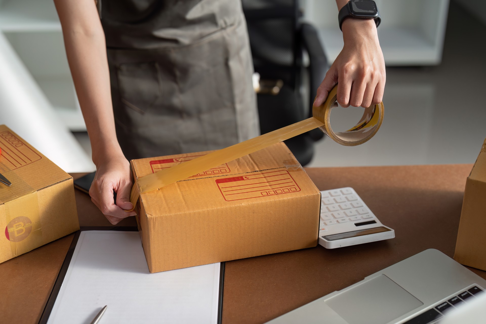 Young business entrepreneur sealing a box with tape. Preparing for shipping, Packing, online selling, e-commerce concept